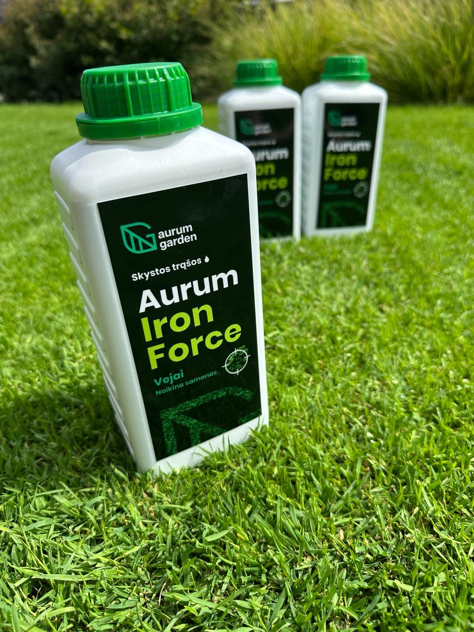 ALT tekstas: „Aurum Iron Force“ trąšų pakuotė stovi ant vejos. Fone neryškiai matomos kitos produkto pakuotės.