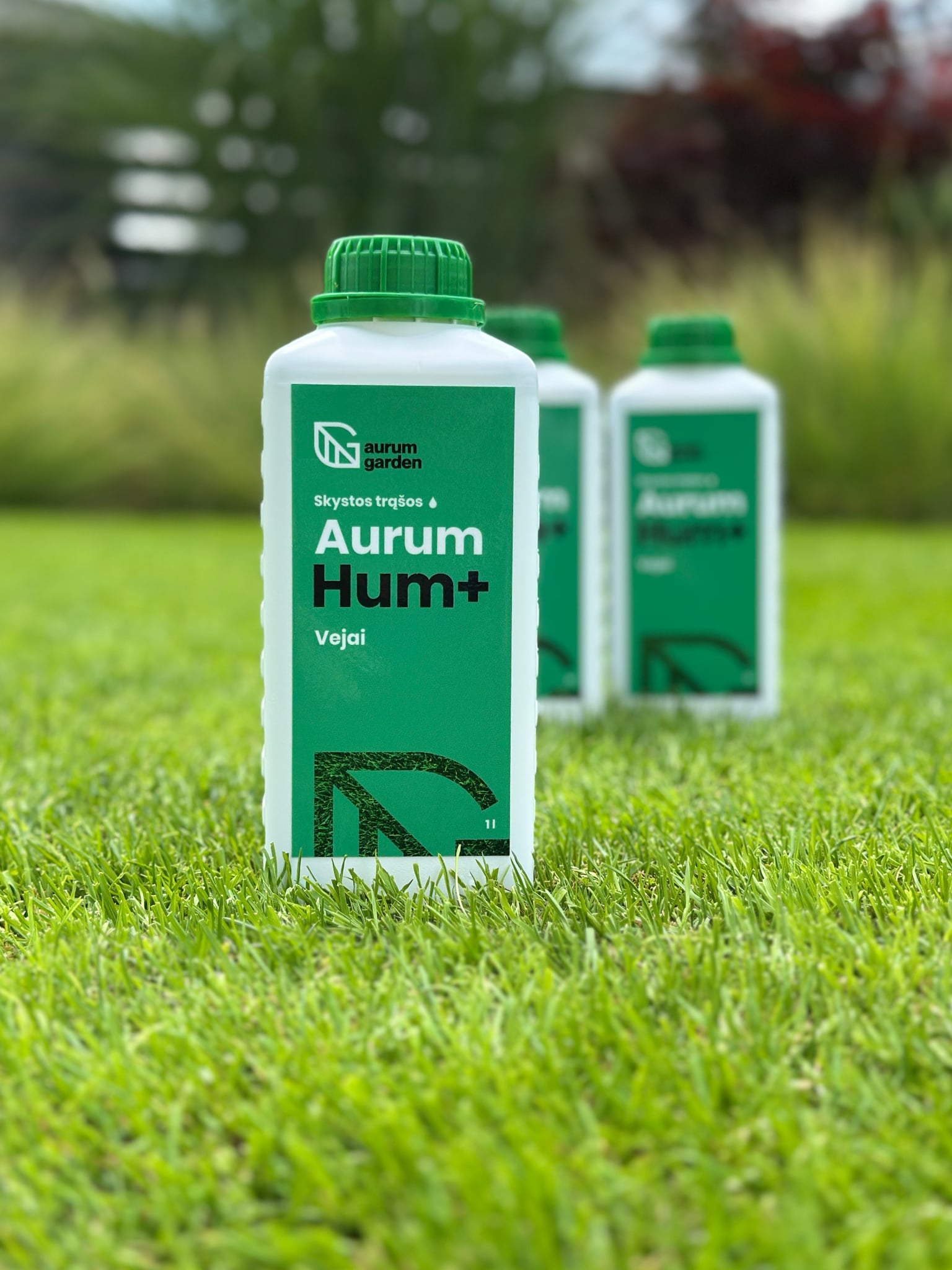 Skystos trąšos vejai "Aurum Hum+" pakuotė, stovinti ant tankios žalios vejos.